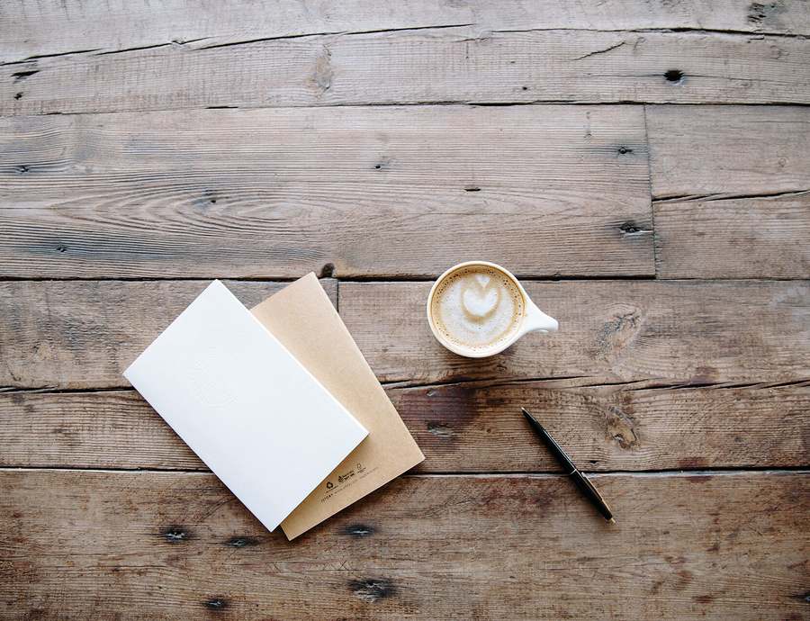 Buku catatan, pena, dan kopi di atas meja kayu